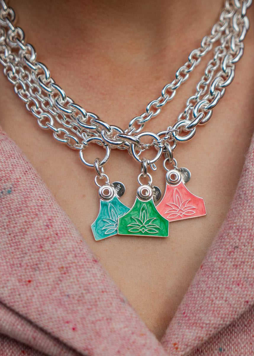 Close-up of a person wearing a silver chain necklace with colorful charms against a pink textured background.